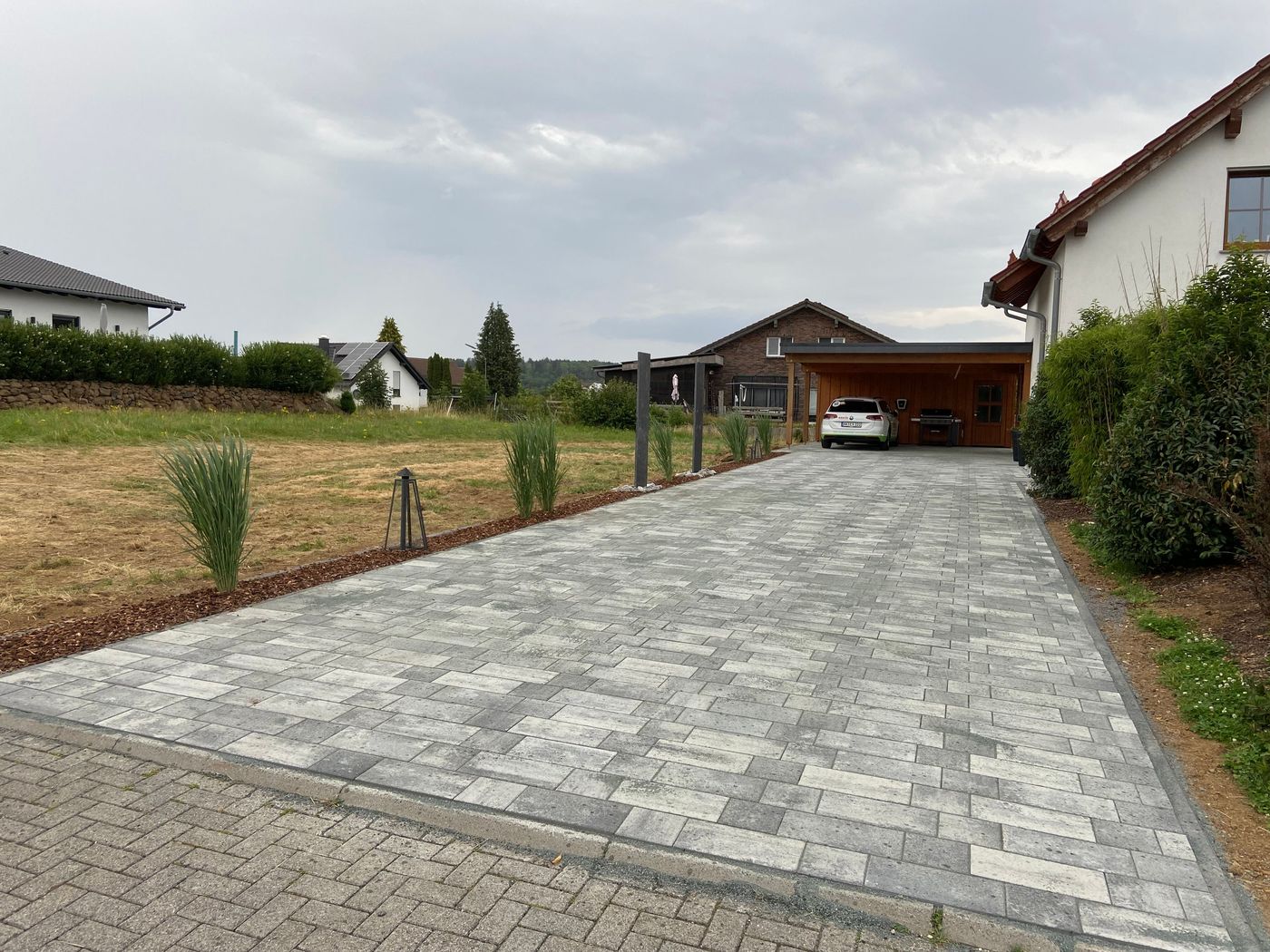 Einfahrt nach der Pflasterung: fertig verlegtes Betonpflaster vor dem Carport